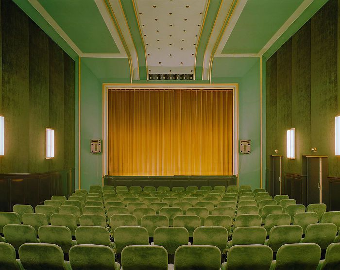 A quiet green auditorium of empty seats facing a stage