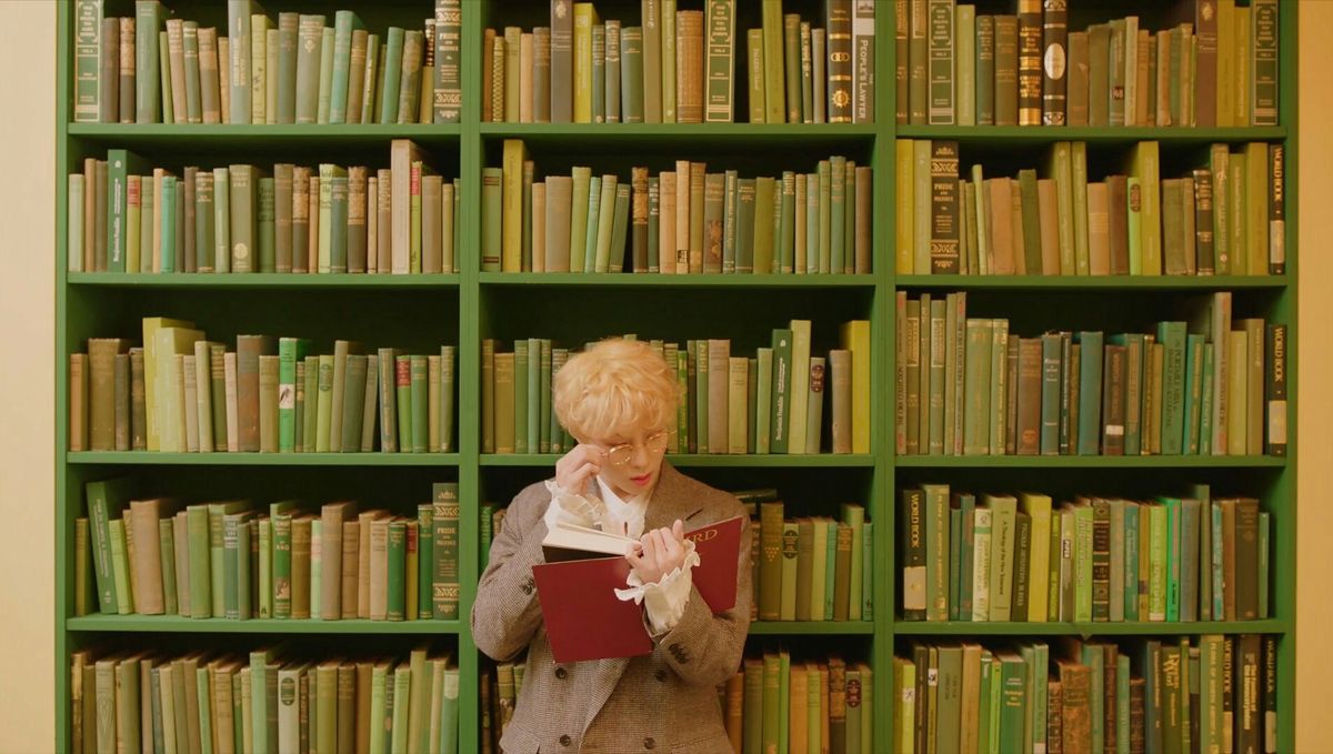 A person reading in front of a wall of green books